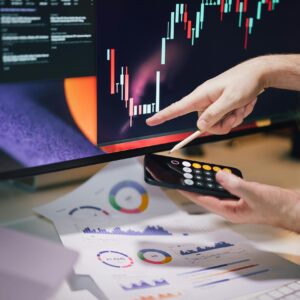 Hands analyzing stock market data on monitor and smartphone in office setting.