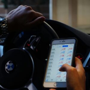 Person using mobile phone for currency trading while driving BMW car.